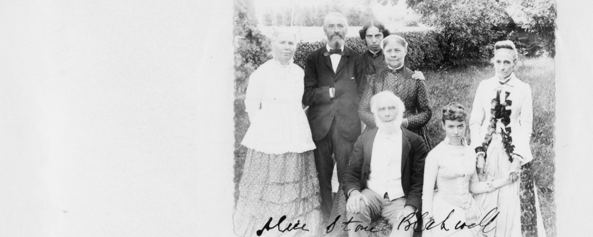 This black and white photograph probably shows (back row, left to right): Dr. Emily Blackwell, Mr. Ainsworth Spofford, Alice Stone Blackwell, and Lucy Stone; (front row, left to right): Henry Browne Blackwell, Florence Spofford and Mrs. Sarah (Partridge). Photo taken sometime between 1880-1893. The family are well dressed, but their clothing and hair are not overly ornate. Most of the women wear floral printed cottons and the men wear suits and ties typical of the period.