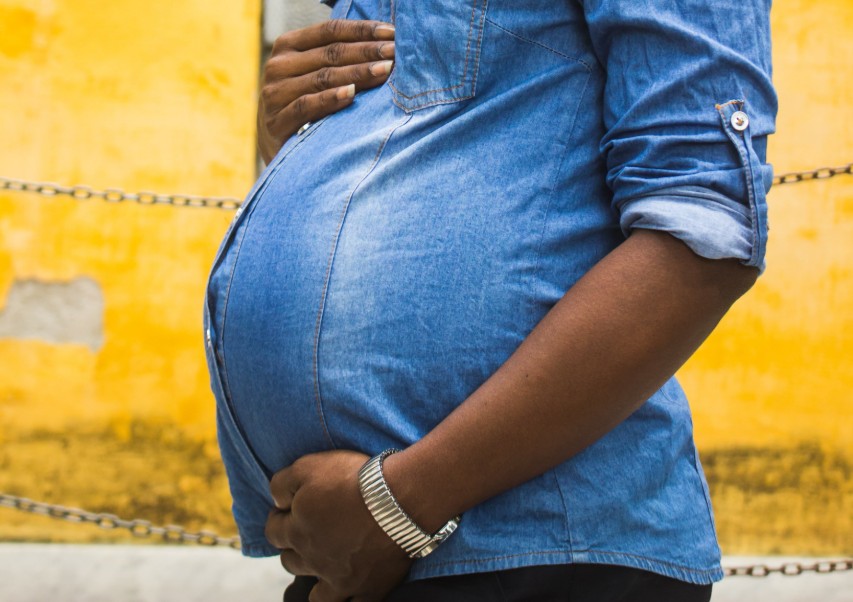 Black woman with a blue demin shirt holding her pregnant belly