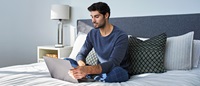 Man sitting on bed looking at laptop