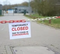 A sign hanging from a red and white chain that says "temporarily closed due to COVID-19